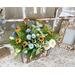 A handmade wooden moose planter. It holds a faux flower arrangement with greenery, peonies, and wildflowers. It sits in an entryway. 